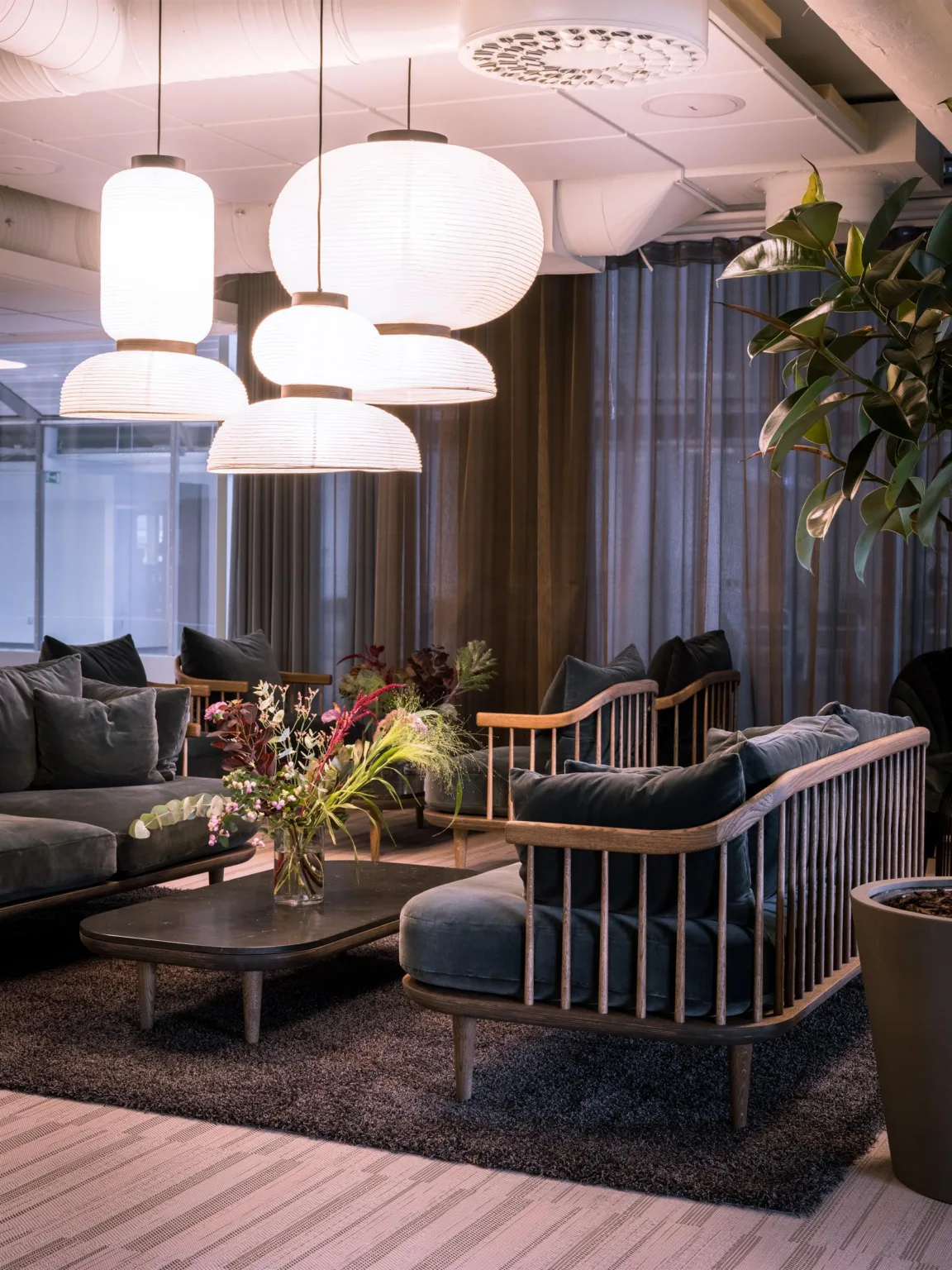 En lounge med soffor och fåtöljer, stora vita lampor och växter omkring.