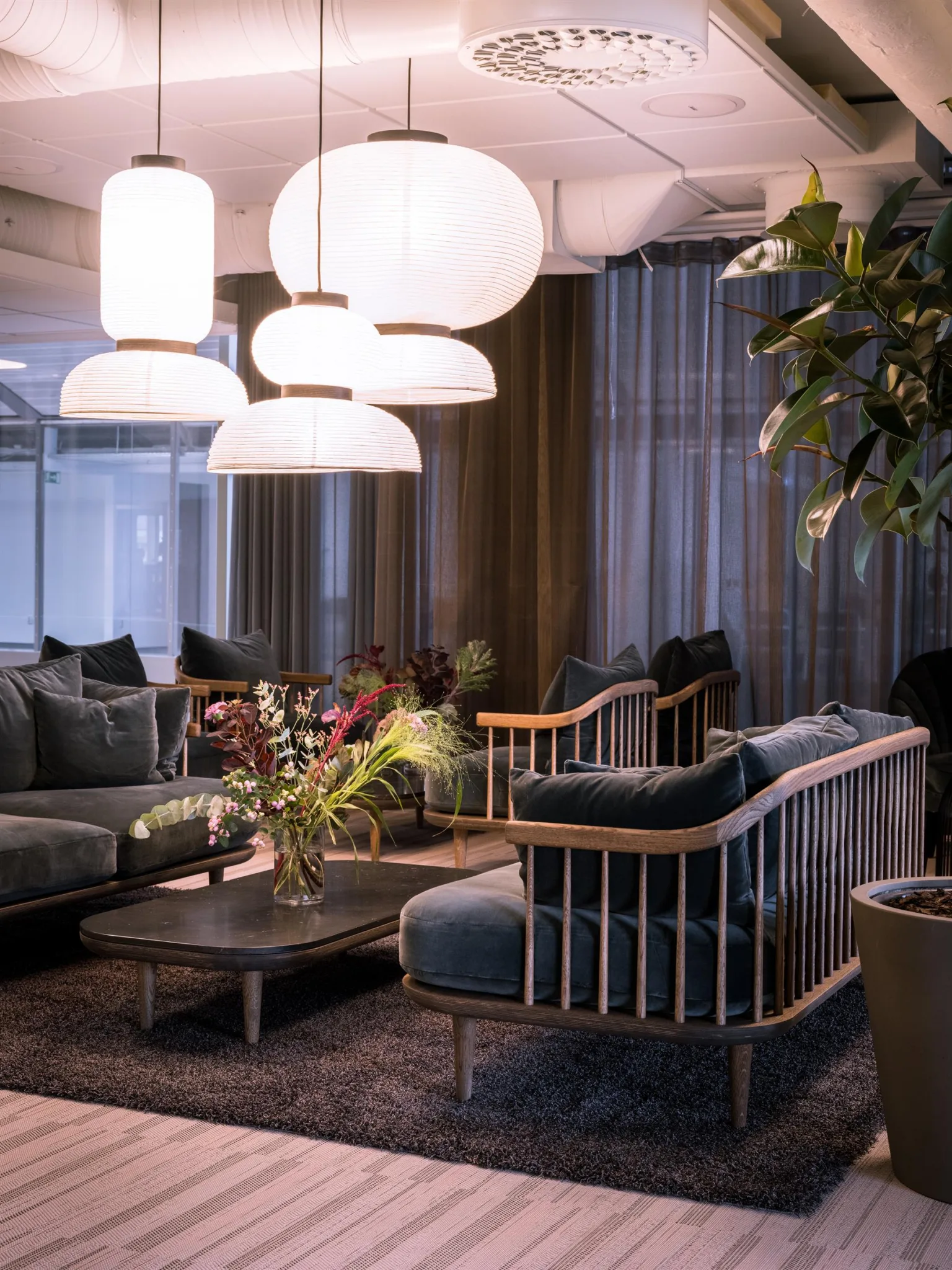 En lounge med soffor och fåtöljer, stora vita lampor och växter omkring.