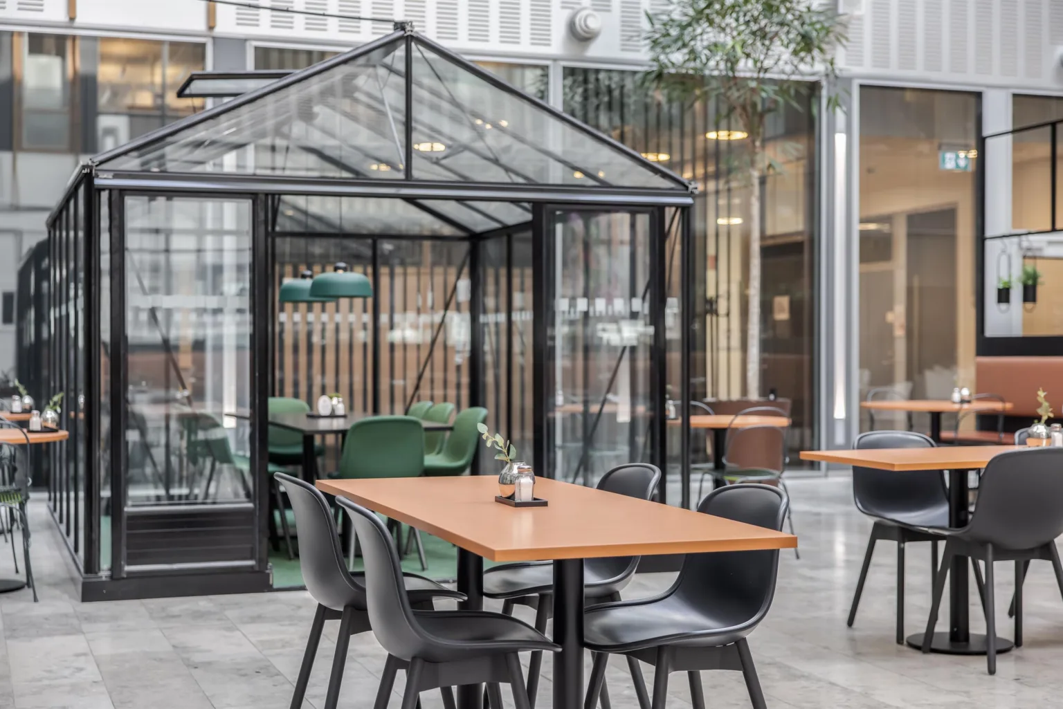 Ett caféområde med bord och stolar, omgiven av en glasvägg med grön inredning.