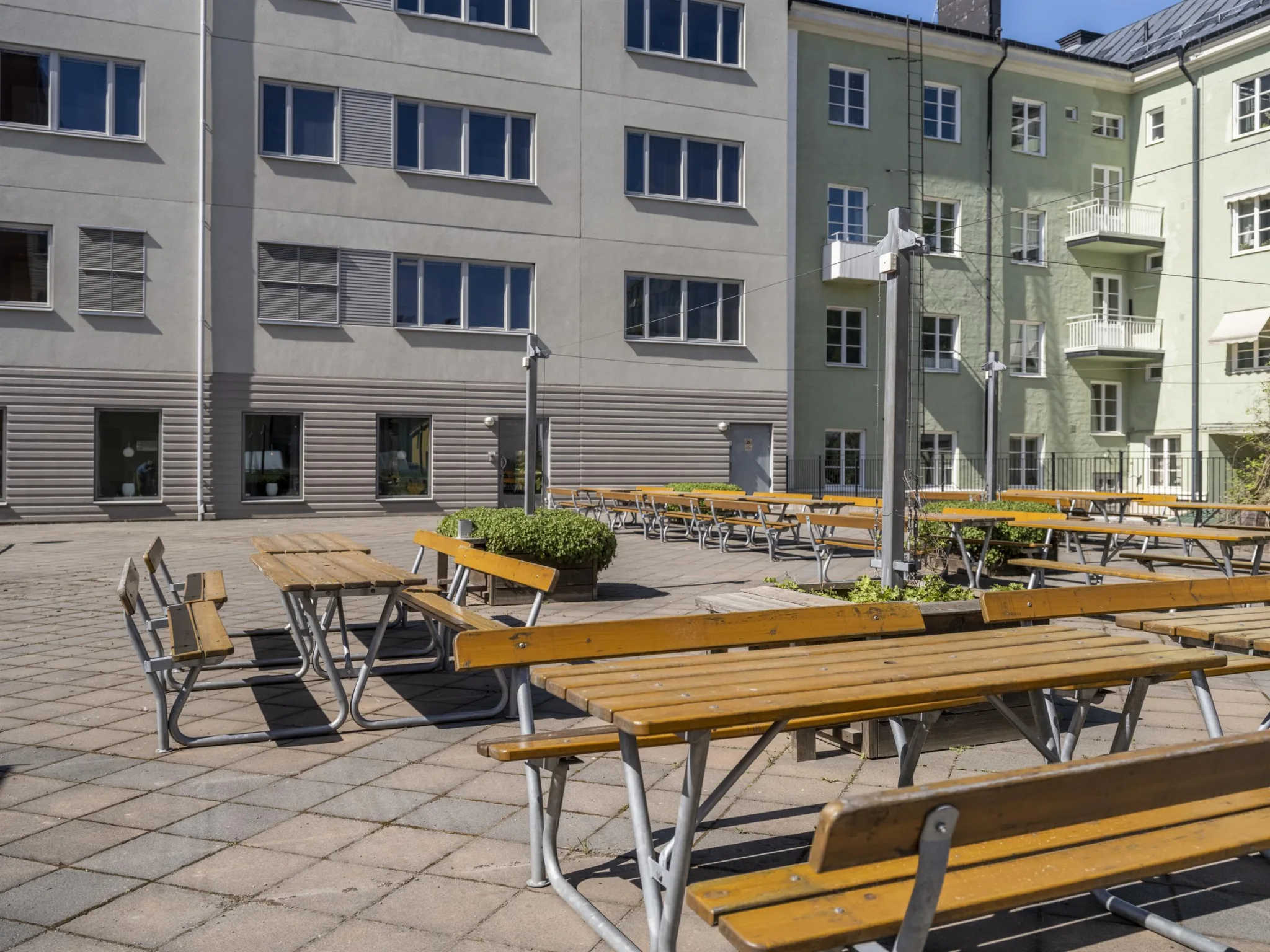 En innergård med träbord och bänkar, omgiven av byggnader i grå och gröna nyanser.