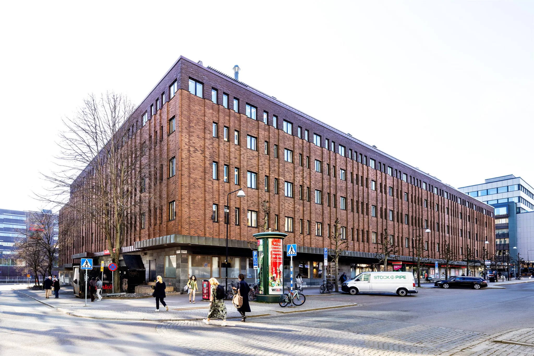 2. Röd tegelbyggnad med flera våningar, omgiven av människor, cyklar och bilar.