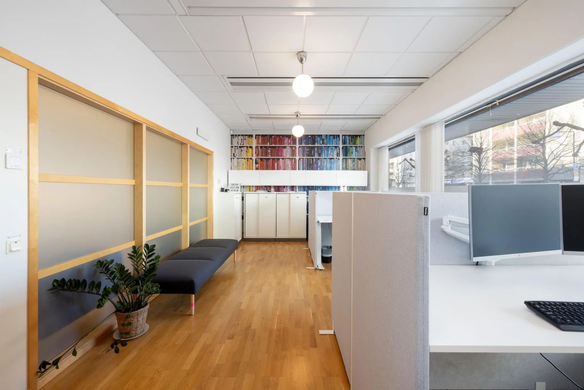 En kontorsyta med vita arbetsstationer, en sittbänk och stora fönster som släpper in ljus.