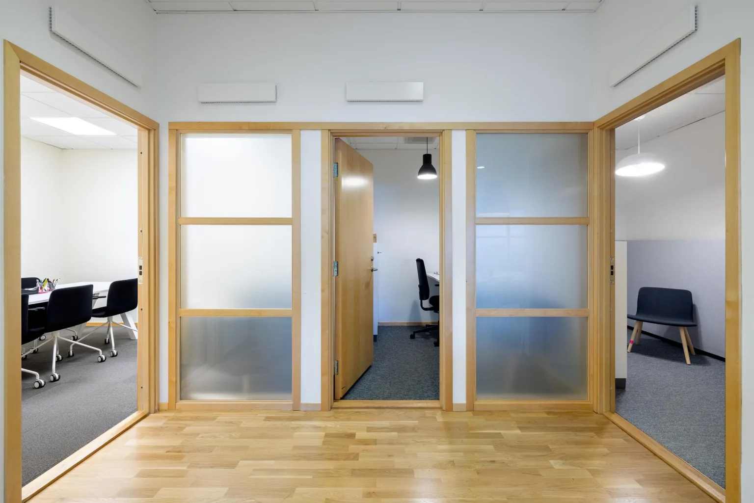 1. Glasväggar med träramar och dörrar som leder in till kontor med skrivbord och stol.