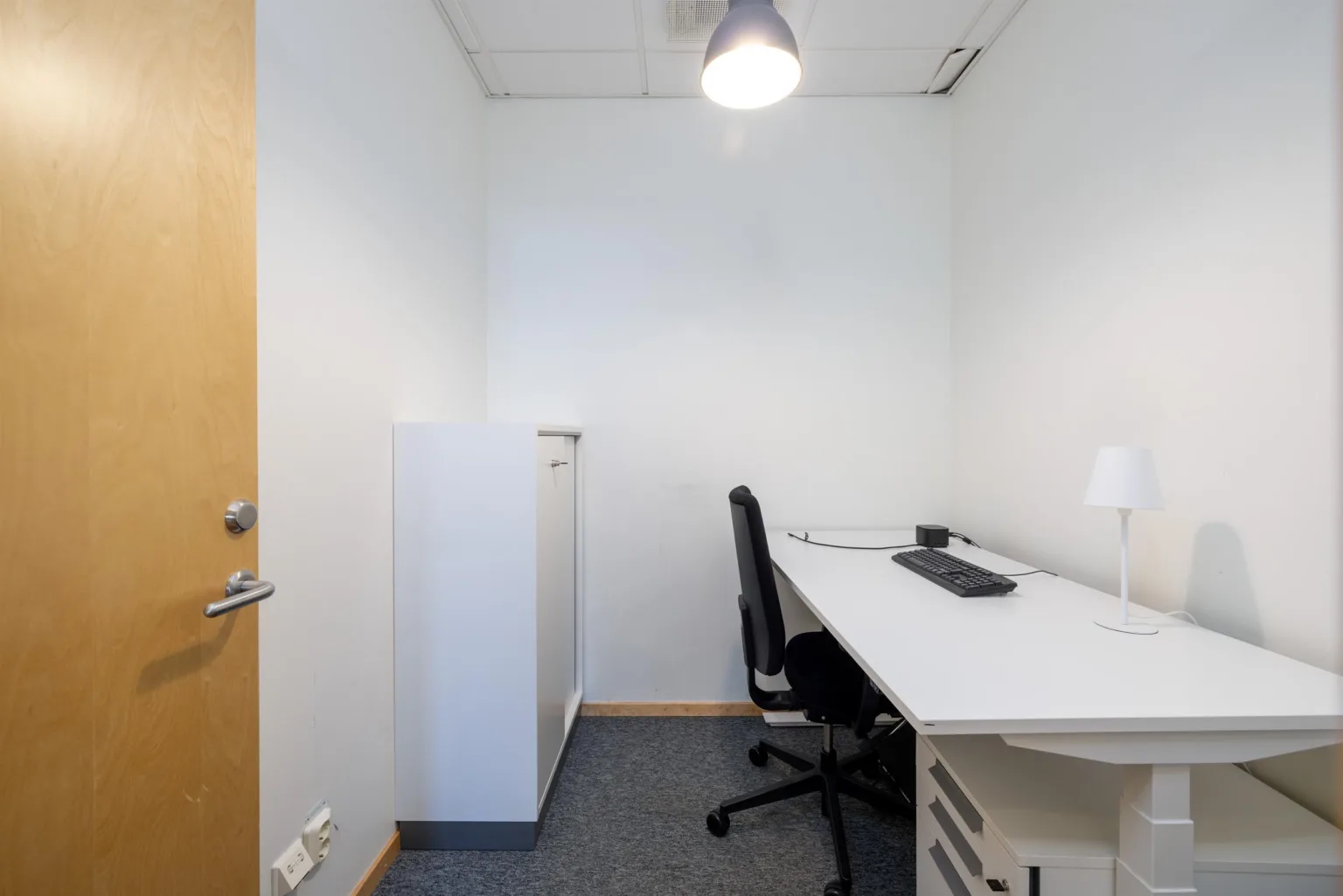 3. Litet kontorsrum med skrivbord, kontorsstol, lampa och tangentbord.