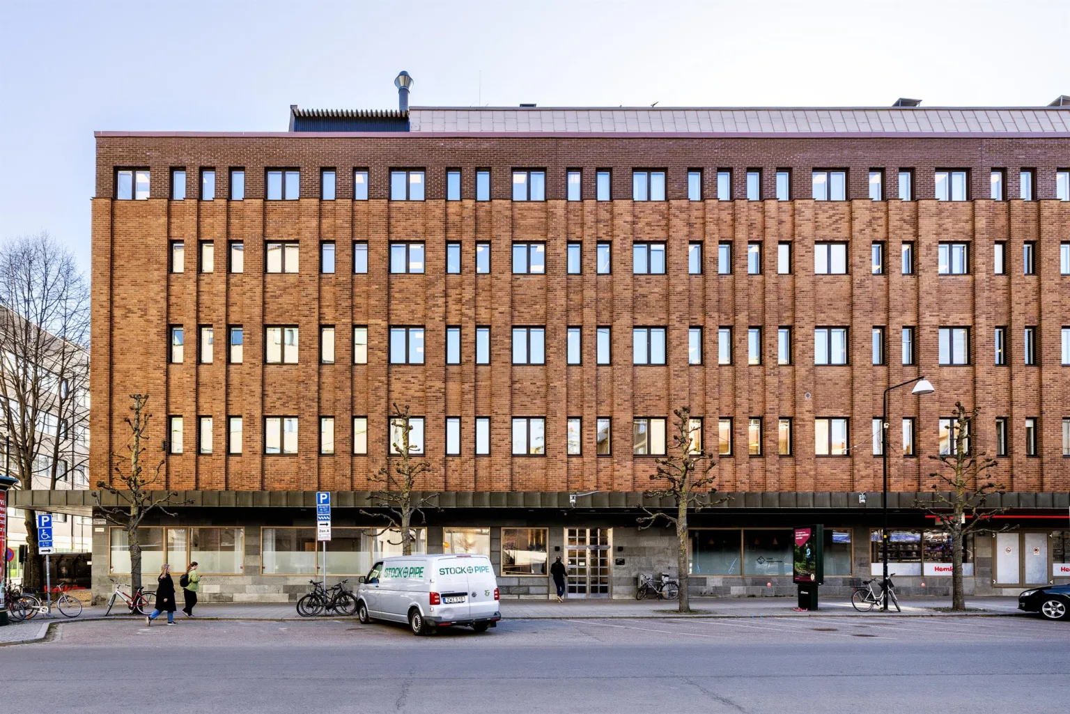 En tegelbyggnad med flera rader av fönster, cyklar och en bil parkerad framför på gatan.