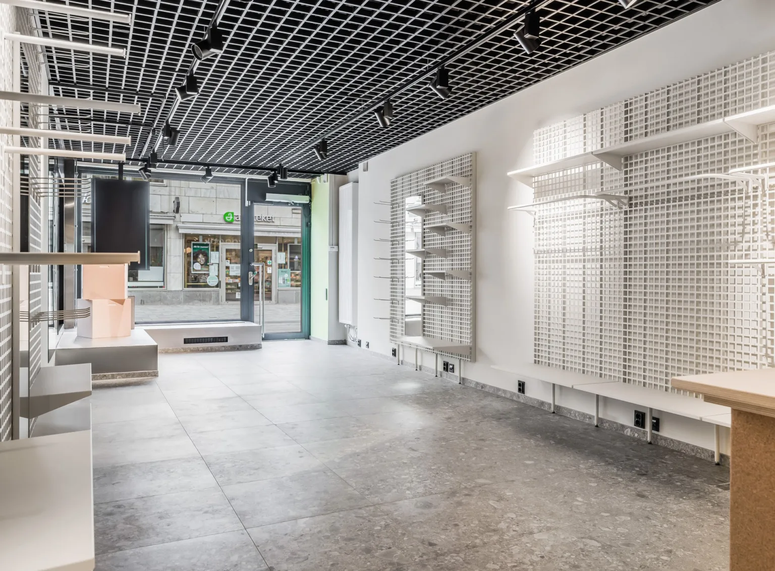 En tom butikslokal med grått golv, svart takgaller och hyllsystem på väggarna.