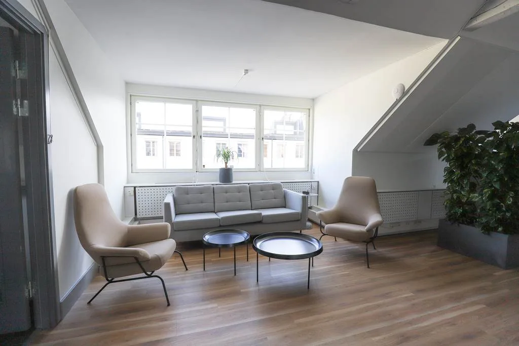 Sittgrupp med soffa, två fåtöljer och små soffbord, placerad vid stora fönster med utsikt.