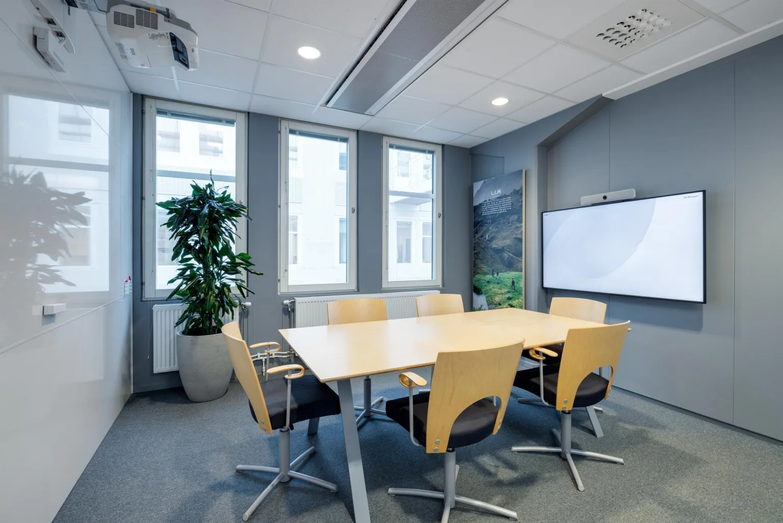 2. Konferensrum med ett stort bord, sex stolar, en växt och en väggmonterad skärm.