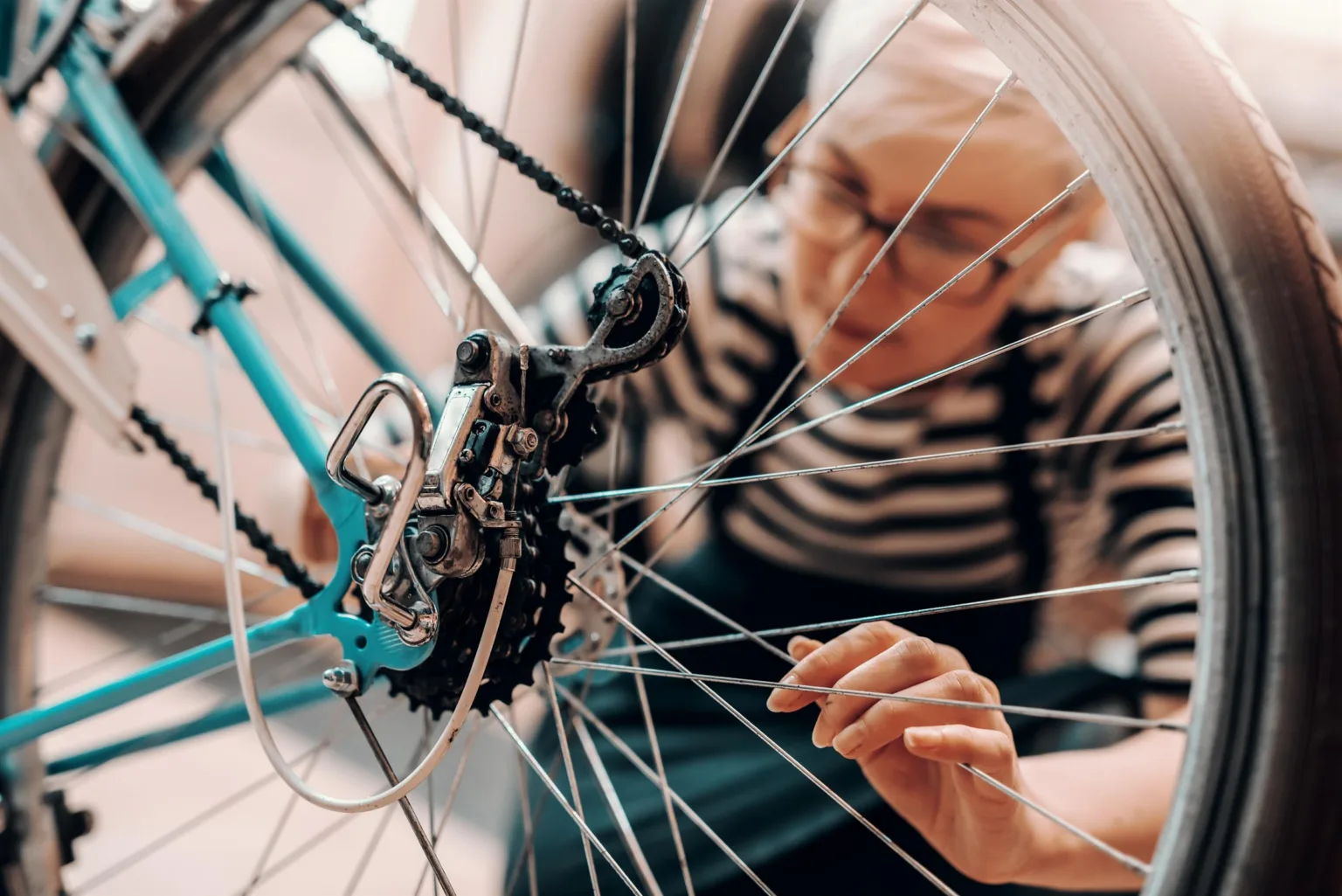 Person i randig tröja justerar kedjan och växlar på en cykel, sedd genom hjulekrarna.