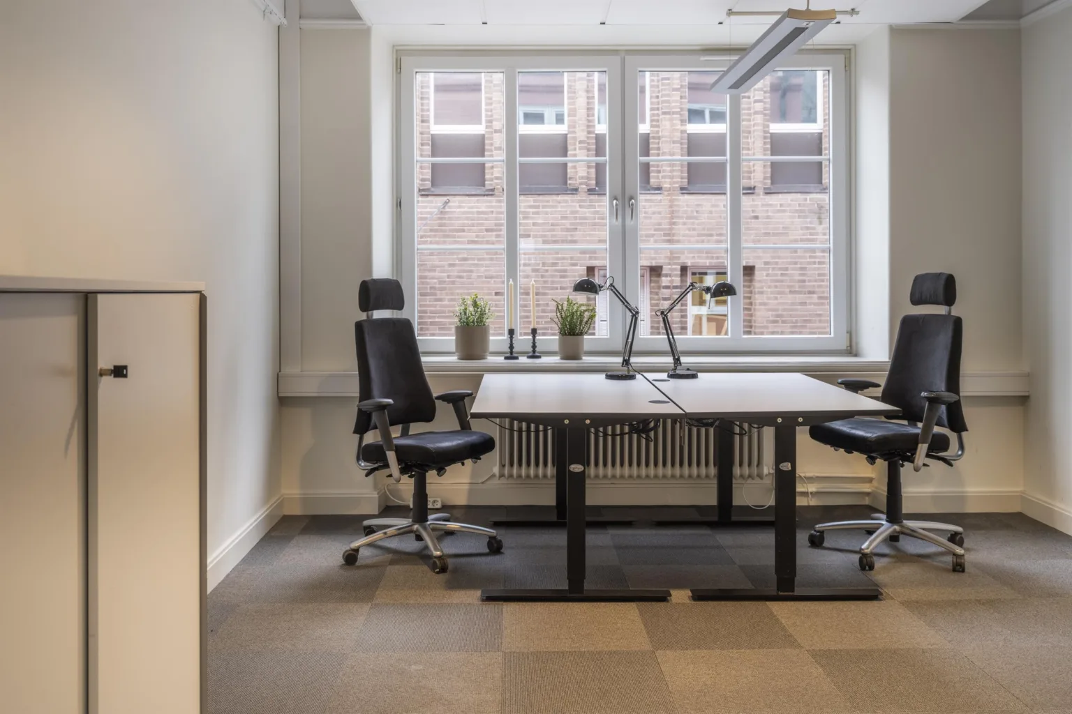 4. Ett kontorsrum med två skrivbord och kontorsstolar framför ett stort fönster.