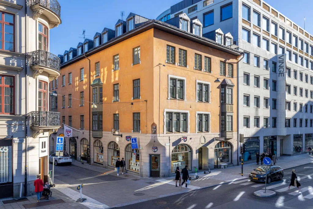 Ett hörnhus med orange fasad och klassiska fönster, omgivet av stadsgator och fotgängare.