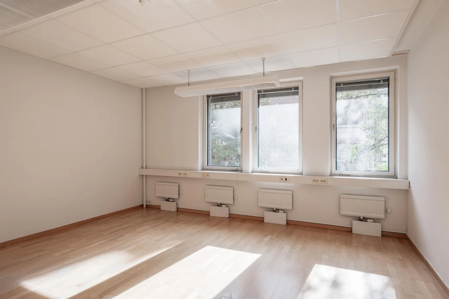 Ett tomt rum med trägolv, vita väggar och tre fönster som släpper in naturligt ljus.