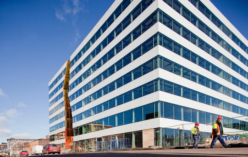 1. En modern byggnad med glasfasad och en högt placerad orange skulptur, arbetare syns nära byggnaden.