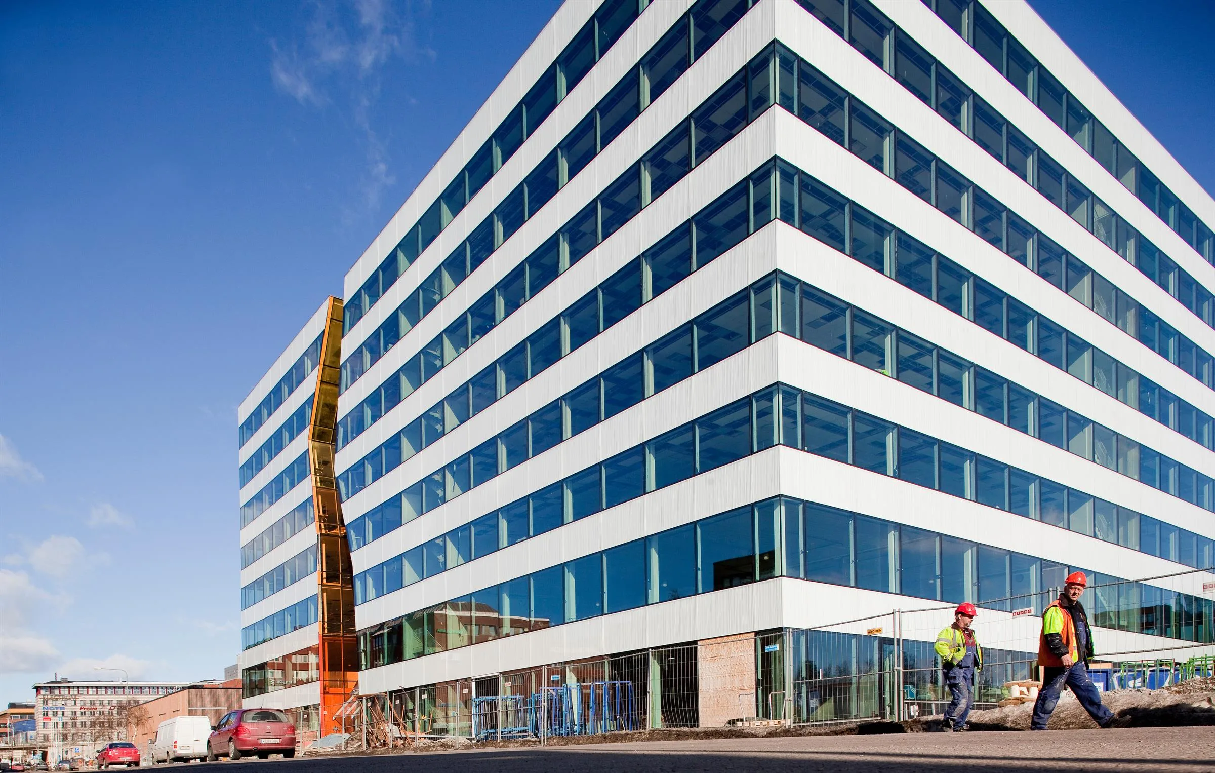 1. En modern byggnad med glasfasad och en högt placerad orange skulptur, arbetare syns nära byggnaden.