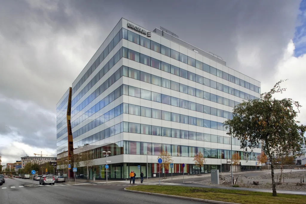 3. En stor modern byggnad med glasfasad, omgiven av träd och en parkeringsplats under en molnig himmel.