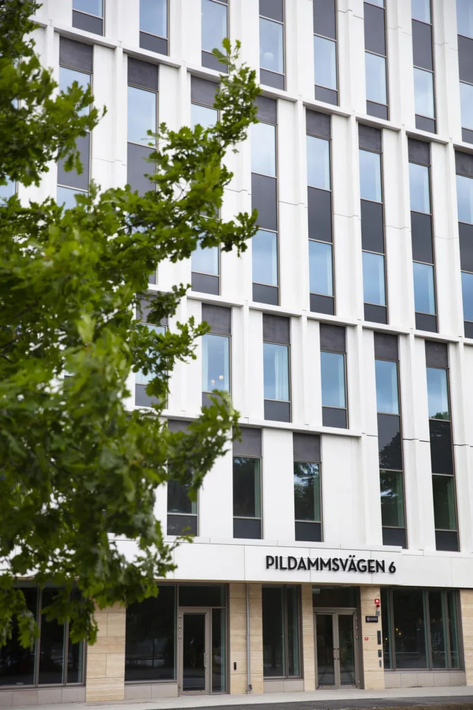 En modern byggnad med vita fasader och stora fönster, texten "Pildammsvägen 4" syns längst ner.