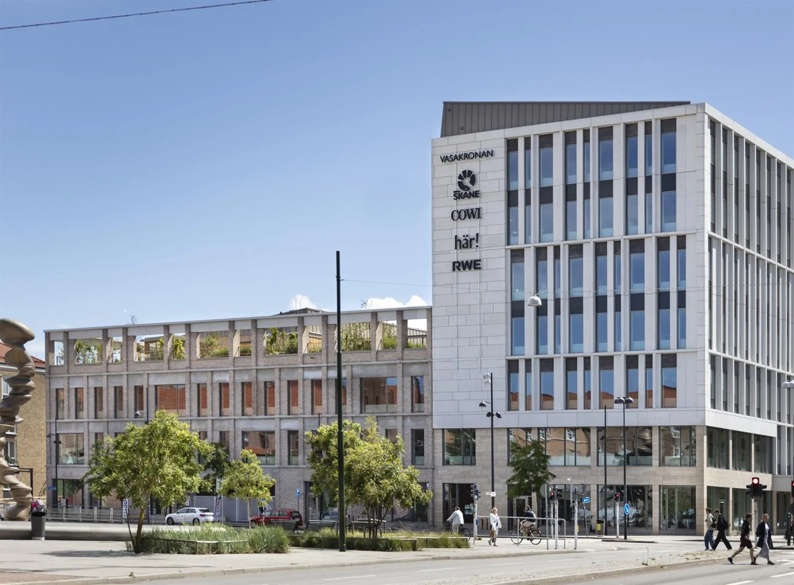 En modern vit byggnad med stora fönster och texten "C/O" synlig på fasaden, omgiven av träd och en bred gata.