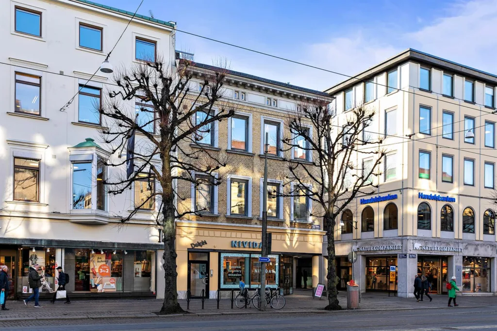 3. Beige byggnad med stora fönster, träd utan löv och butiksskyltar.