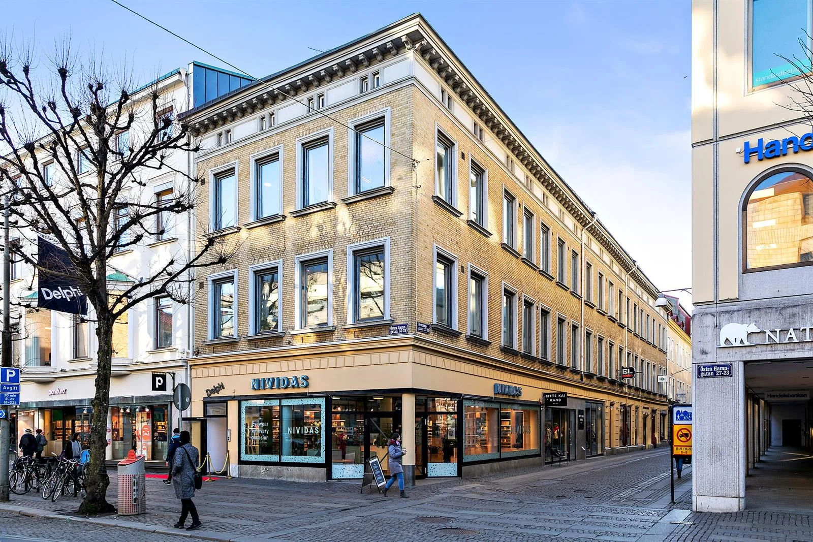 5. Hörnbyggnad i beige med stora fönster och en butik på bottenvåningen.