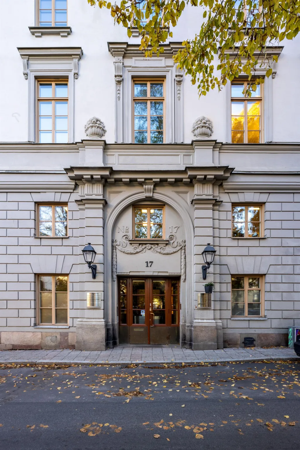 En byggnadsfasad med en välvd entrédörr, detaljerad stenarkitektur och gatulampor.