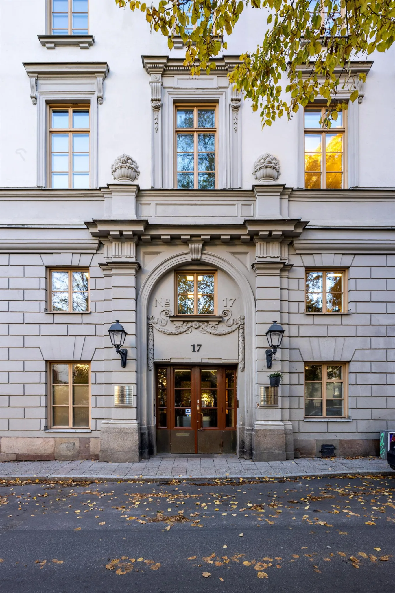En byggnadsfasad med en välvd entrédörr, detaljerad stenarkitektur och gatulampor.