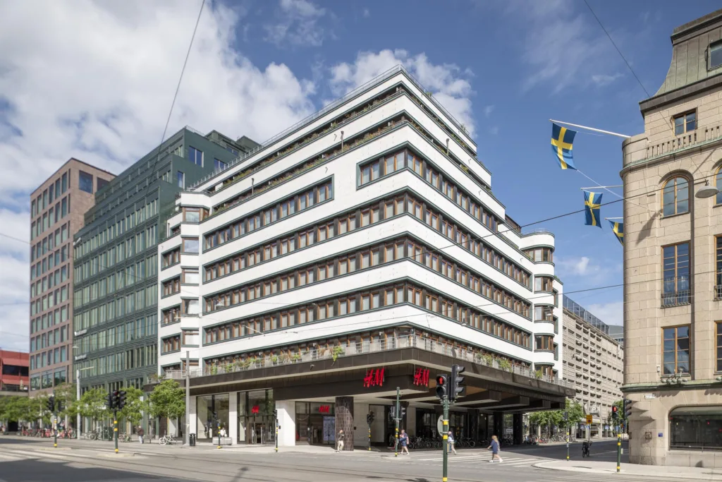 4. Ett modernt hörnhus med vita våningar och stora fönster, svenska flaggor syns i bakgrunden.