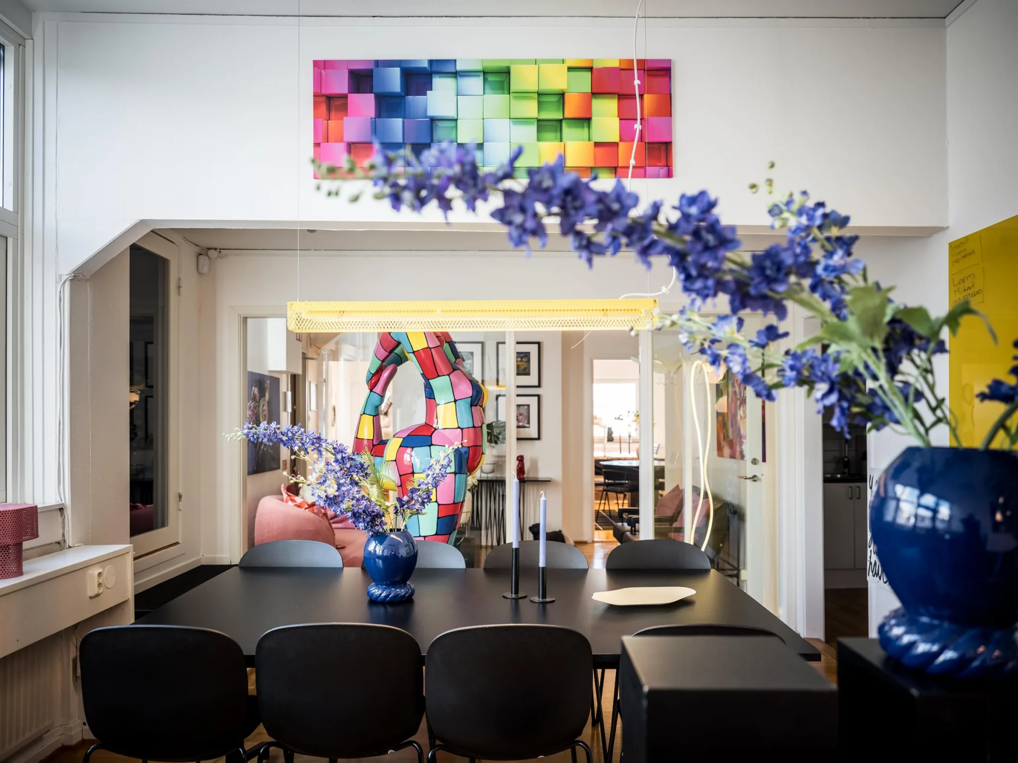 2. Ett matrum med en svart matbord och stolar, dekorerat med en blå vas med lila blommor och en färgglad abstrakt konstverk på väggen.