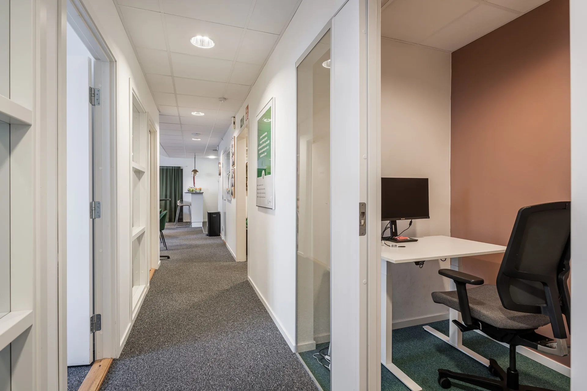4. En kontorskorridor med bås för arbetsplatser, vitmålade väggar och grå matta.
