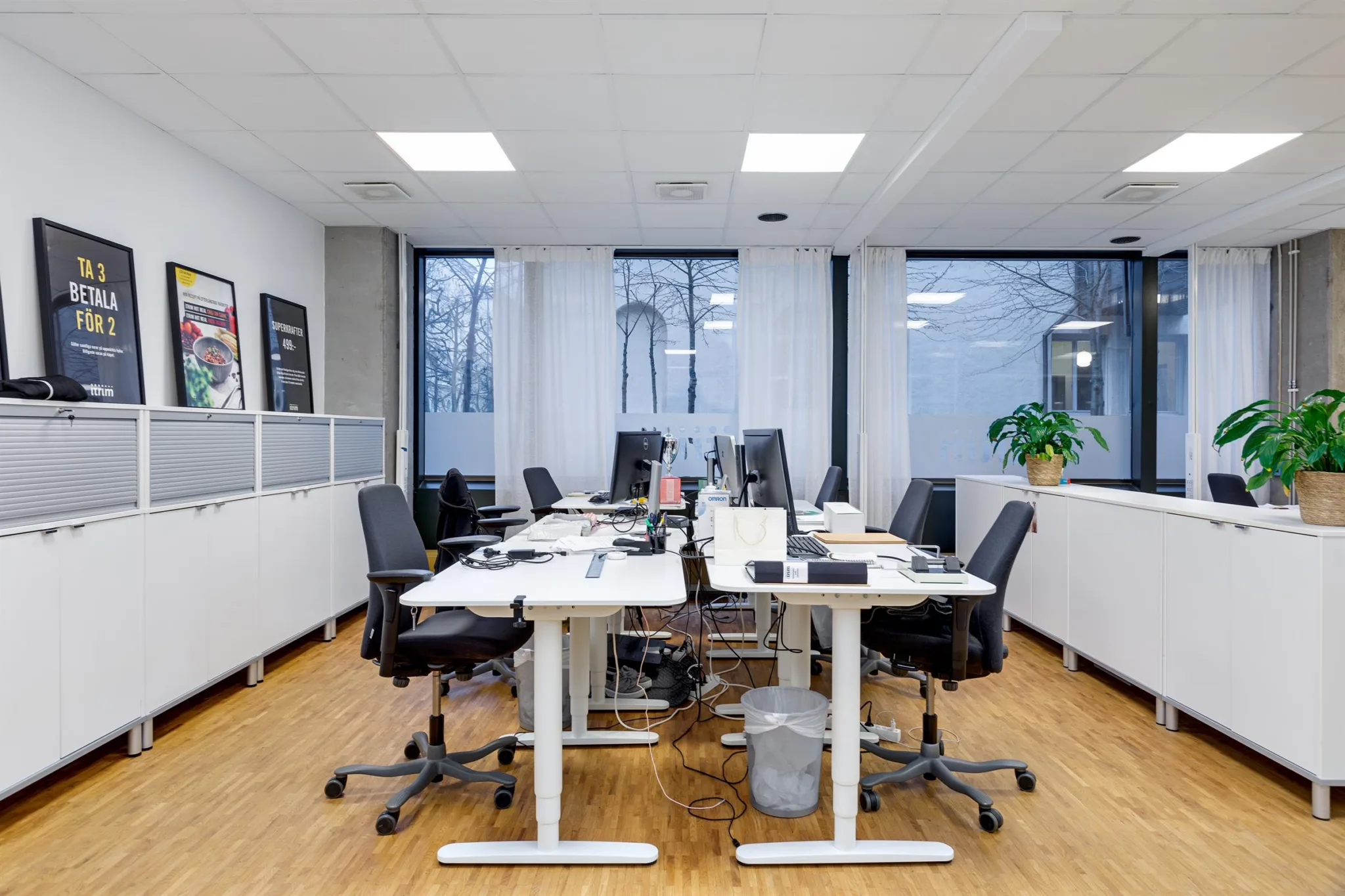 En kontorsmiljö med skrivbord, datorskärmar, kontorsstolar och fönster som vetter mot gatan.