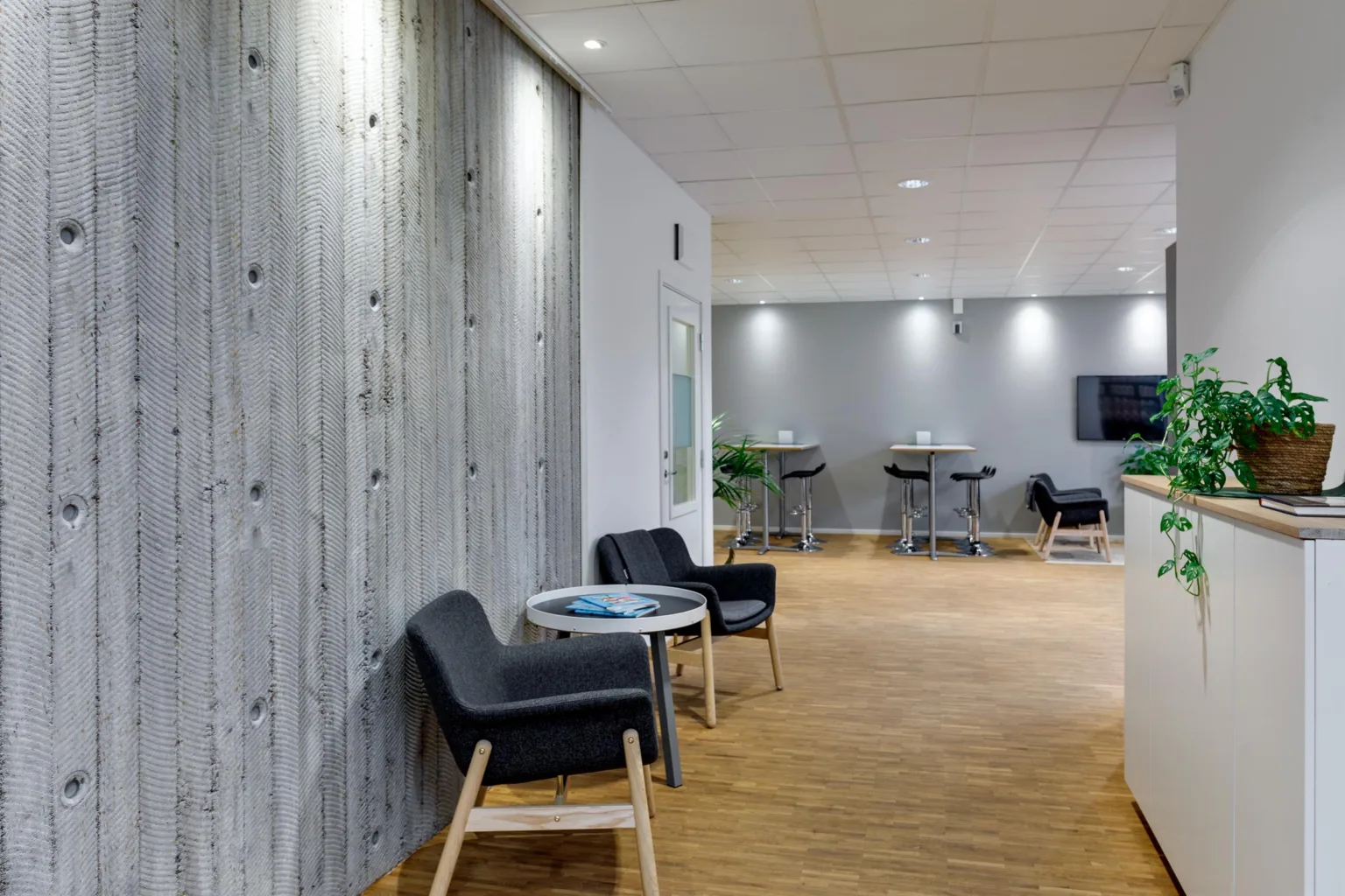 Loungeområde med svarta stolar, små bord och betongväggar.