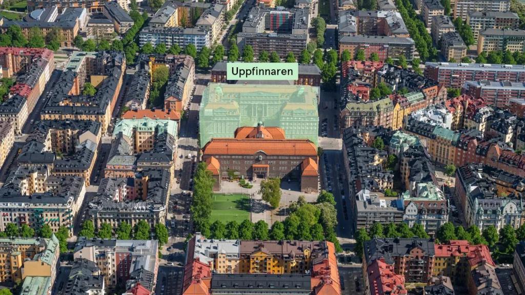 Flygbild över byggnader och grönområden med texten "Uppfinnaren" markerad ovanför en central byggnad.