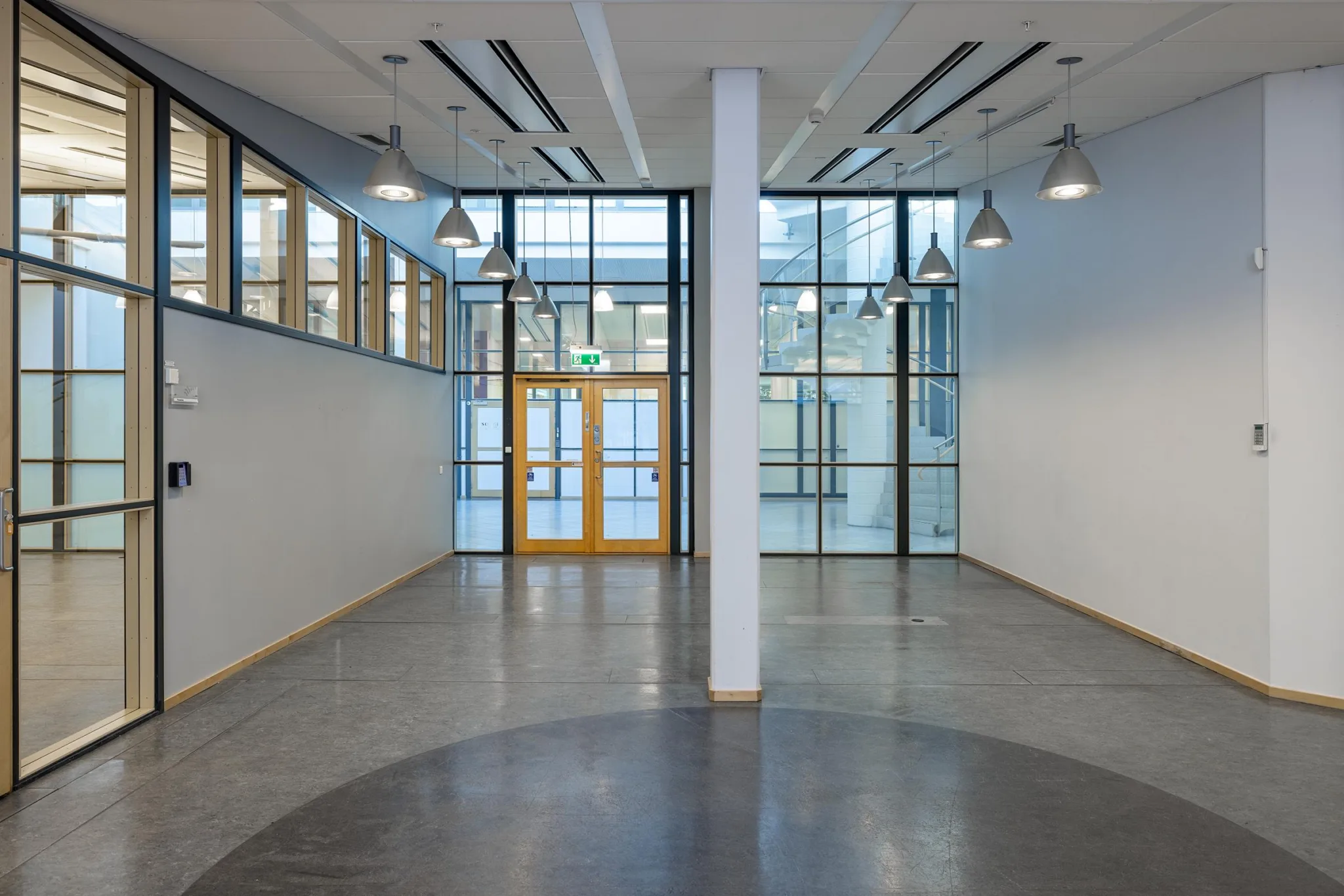 1. En ljus hall med stora glasfönster, vita väggar och ett pelarstöd i mitten.