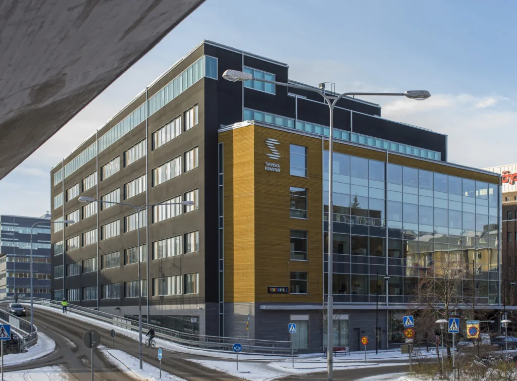 En modern byggnad med stora glaspartier och svart fasad står vid en snötäckt gata.