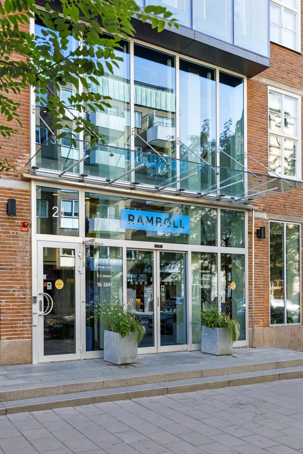En byggnadsfasad med glasentré och skylten "DAHL" ovanför, omgiven av växter.