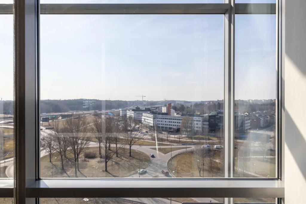 Utsikt genom ett stort fönster mot ett parkområde och byggnader i fjärran.