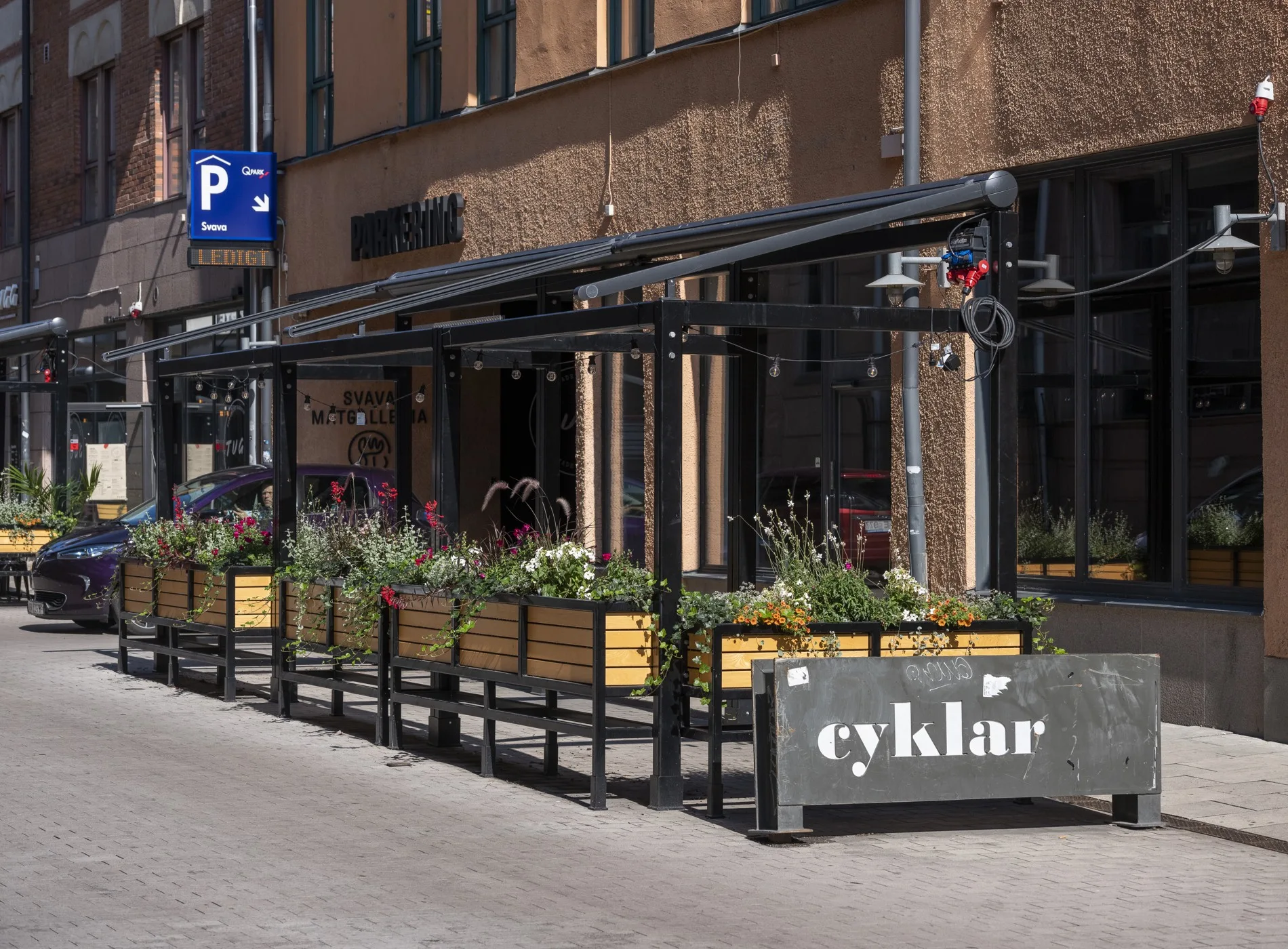 En uteservering med träpaneler och blommor framför en byggnad, med en skylt som lyder "cyklar."