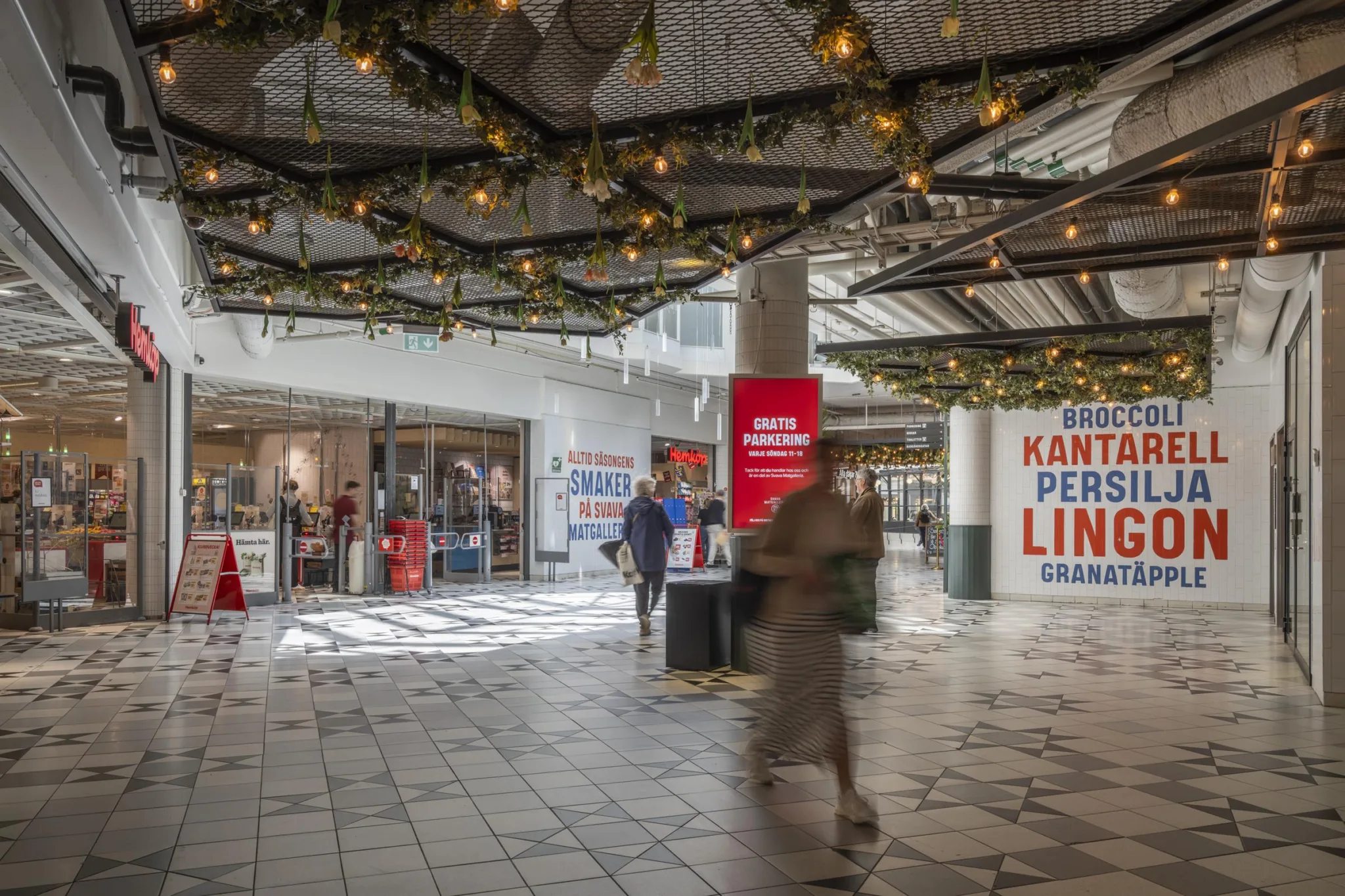 Ett köpcentrum med grön takdekoration och flera skyltar, inklusive en röd skylt med texten "KANTER PERSON LINDEX."