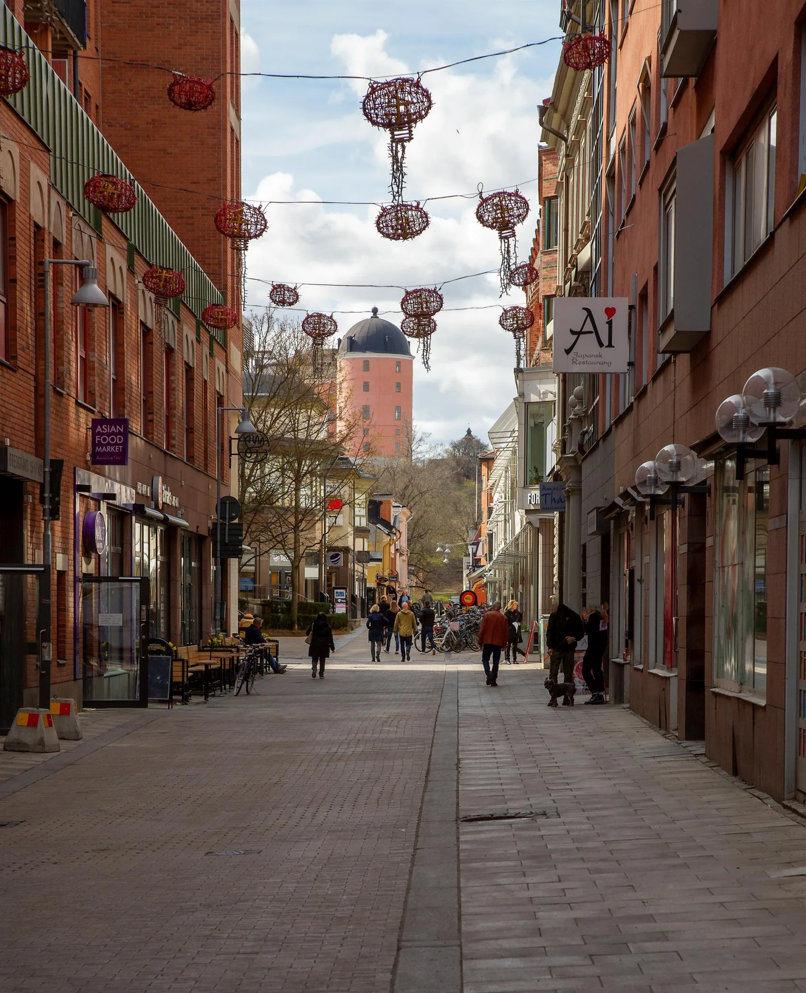 En gågata med röda byggnader på båda sidor, dekorerad med röda lyktor som hänger i luften.