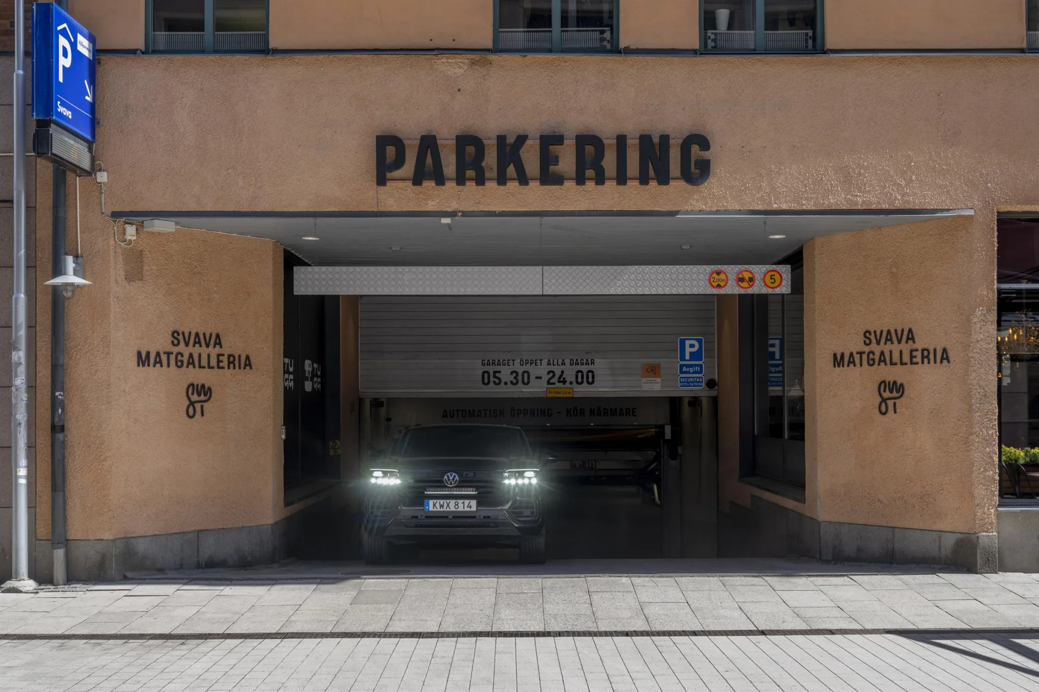 En bil kör ut från en parkeringsgarage med texten "PARKERING" ovanför ingången.