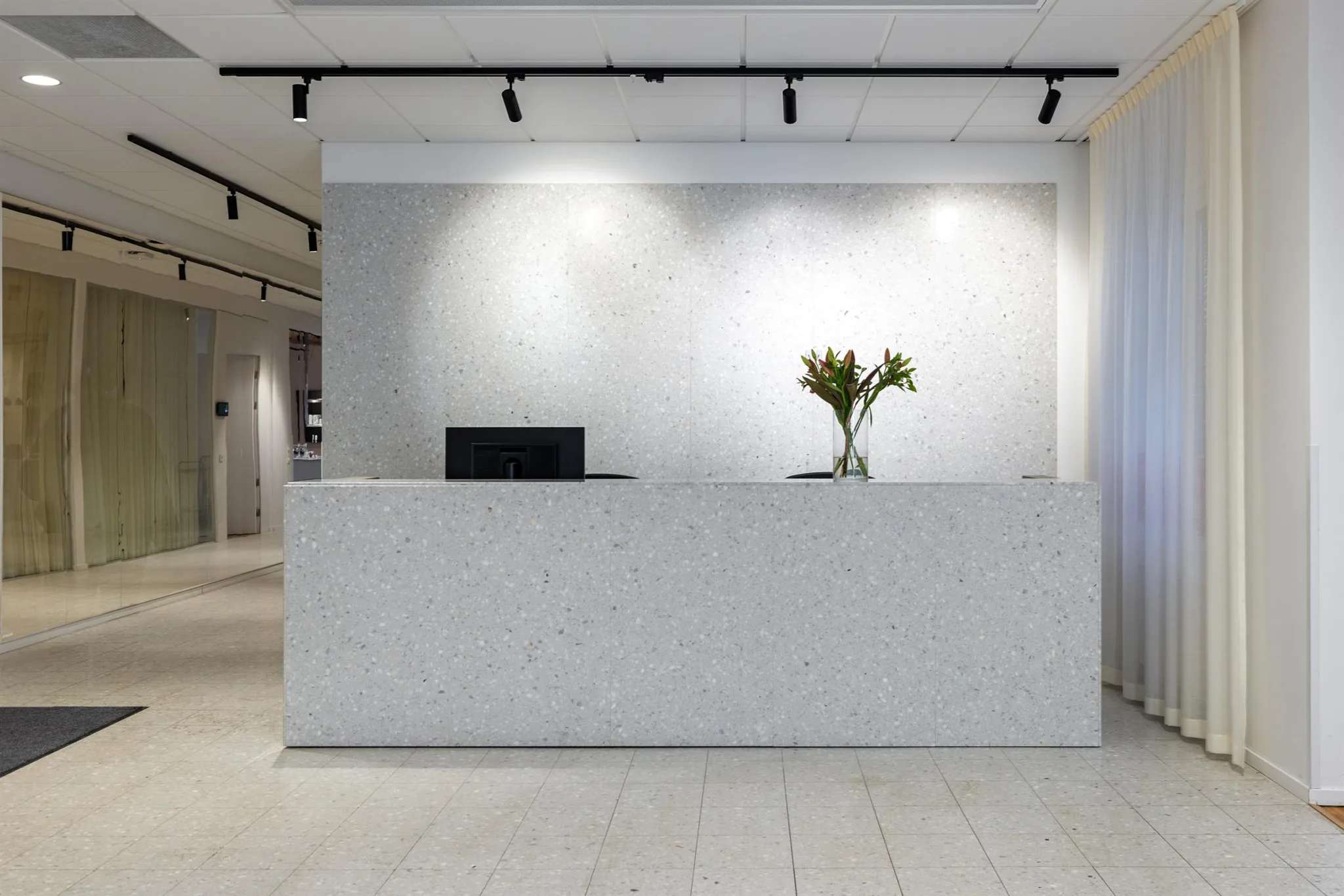 En reception med en vit disk, en datorskärm och en vas med blommor.