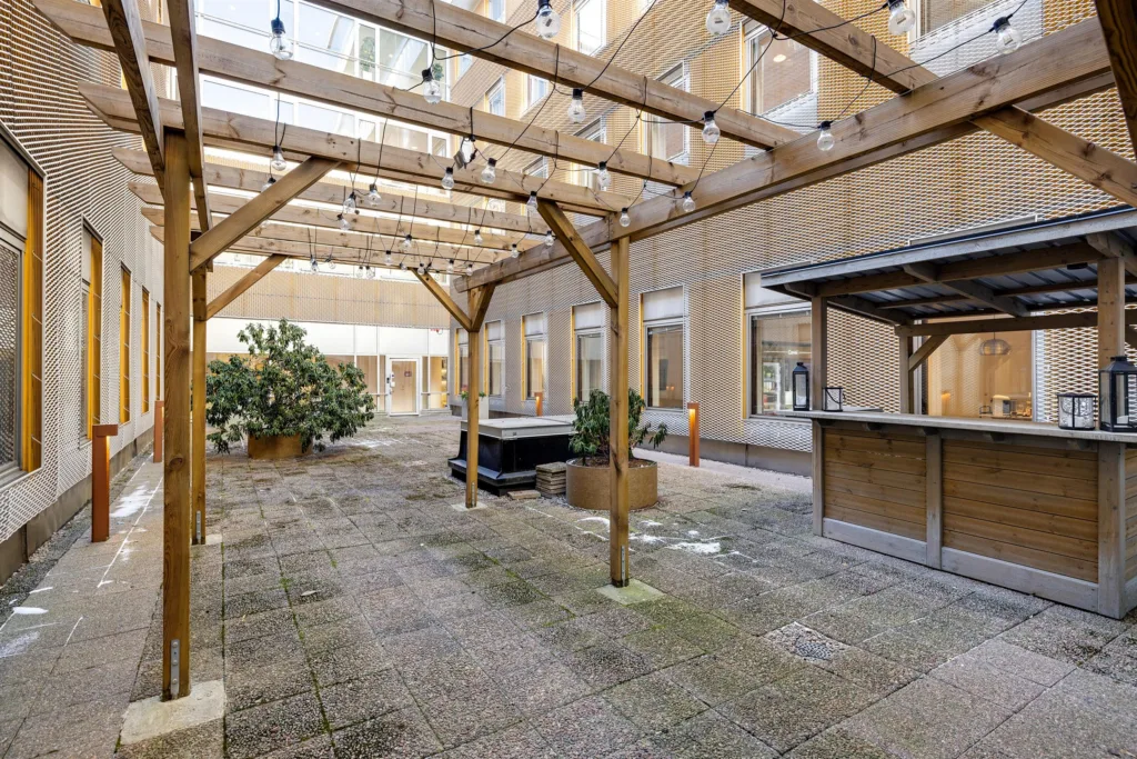 En innergård med träpergola, ljusdekorationer och ett litet barområde.