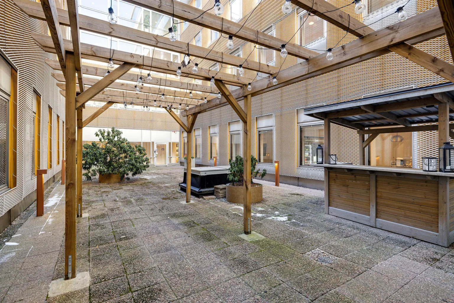 En innergård med träpergola, ljusdekorationer och ett litet barområde.