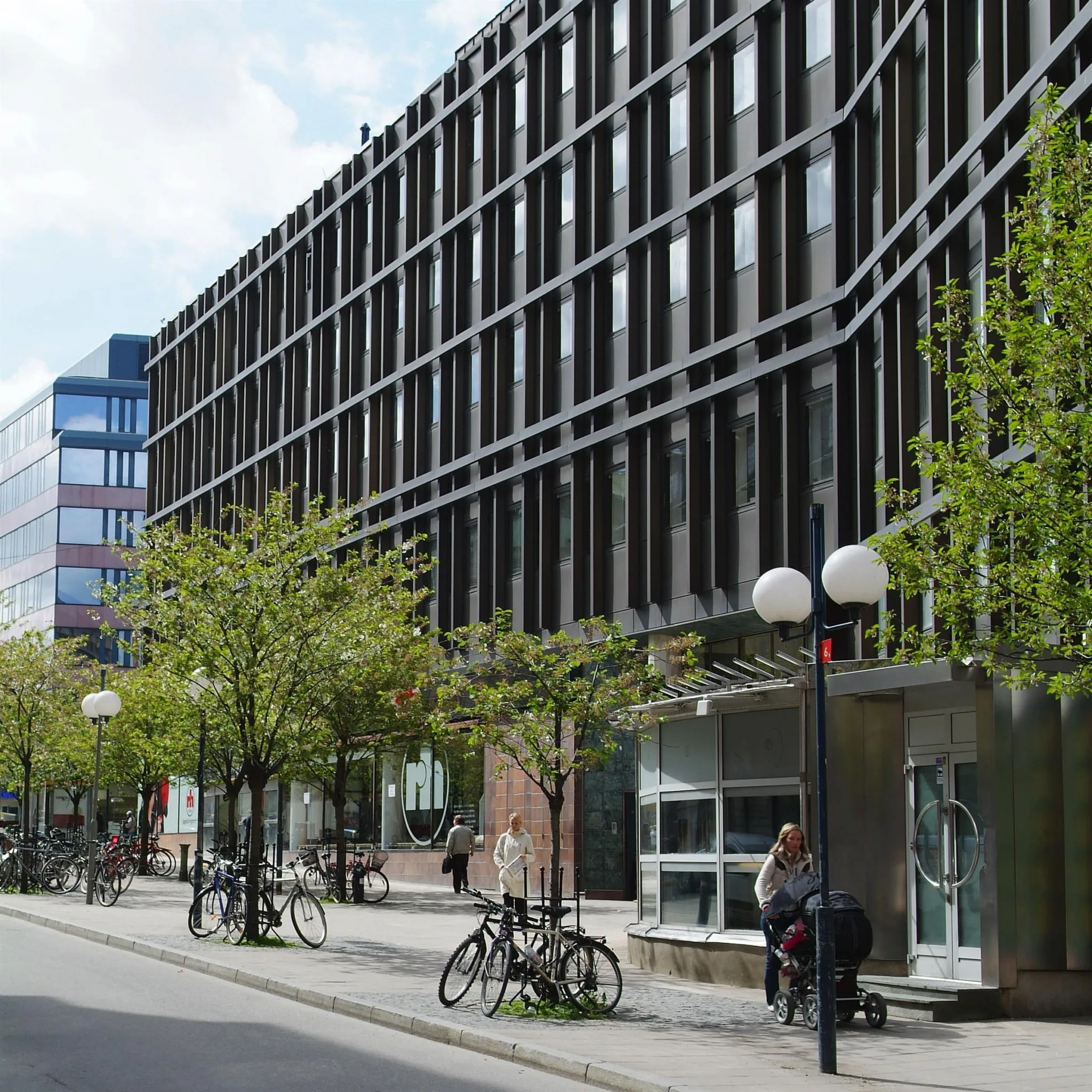 En gata med moderna byggnader, cyklar vid trottoaren och träd längs vägen.