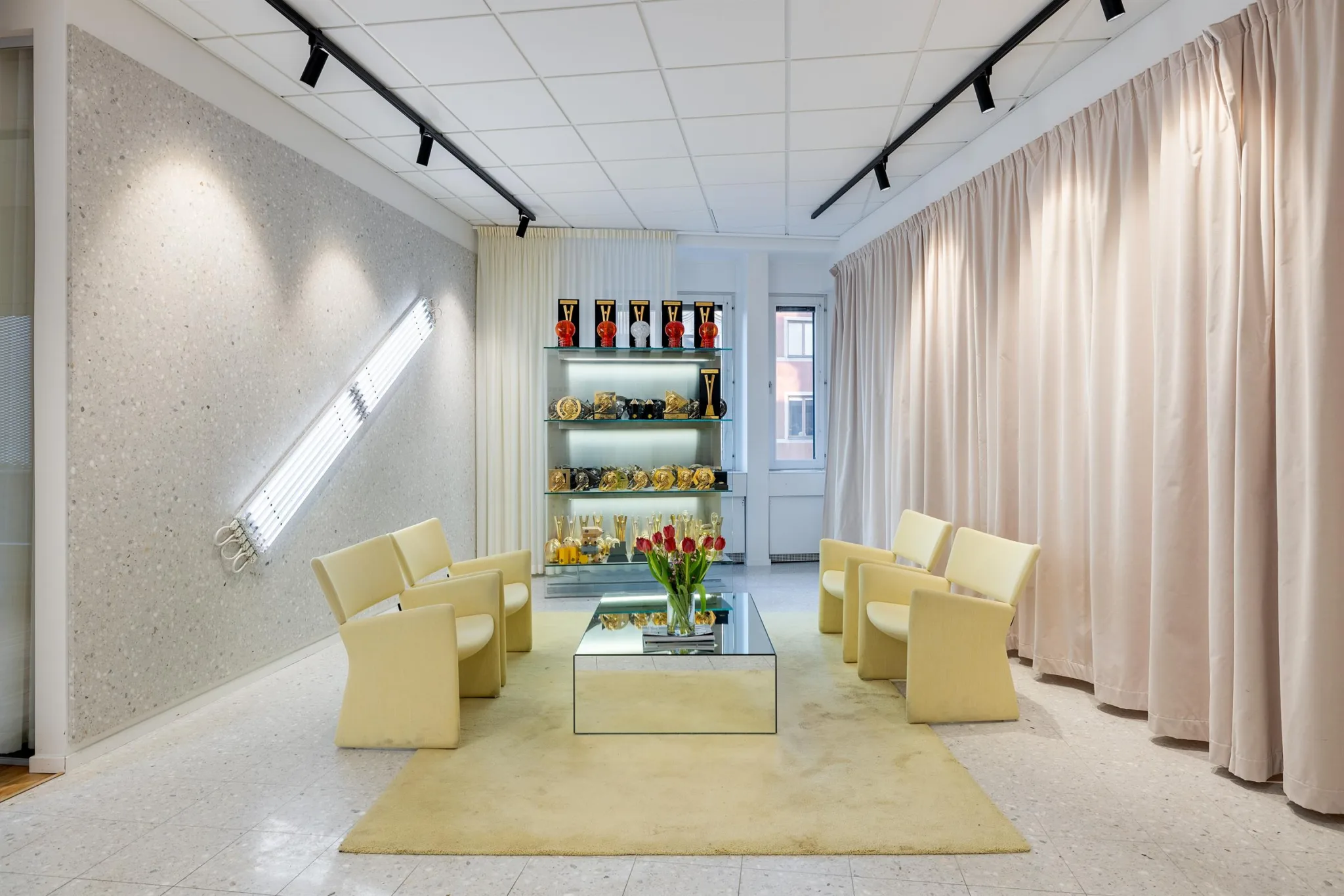 Modern lounge med fyra gula fåtöljer runt ett glasbord, hyllor i bakgrunden.
