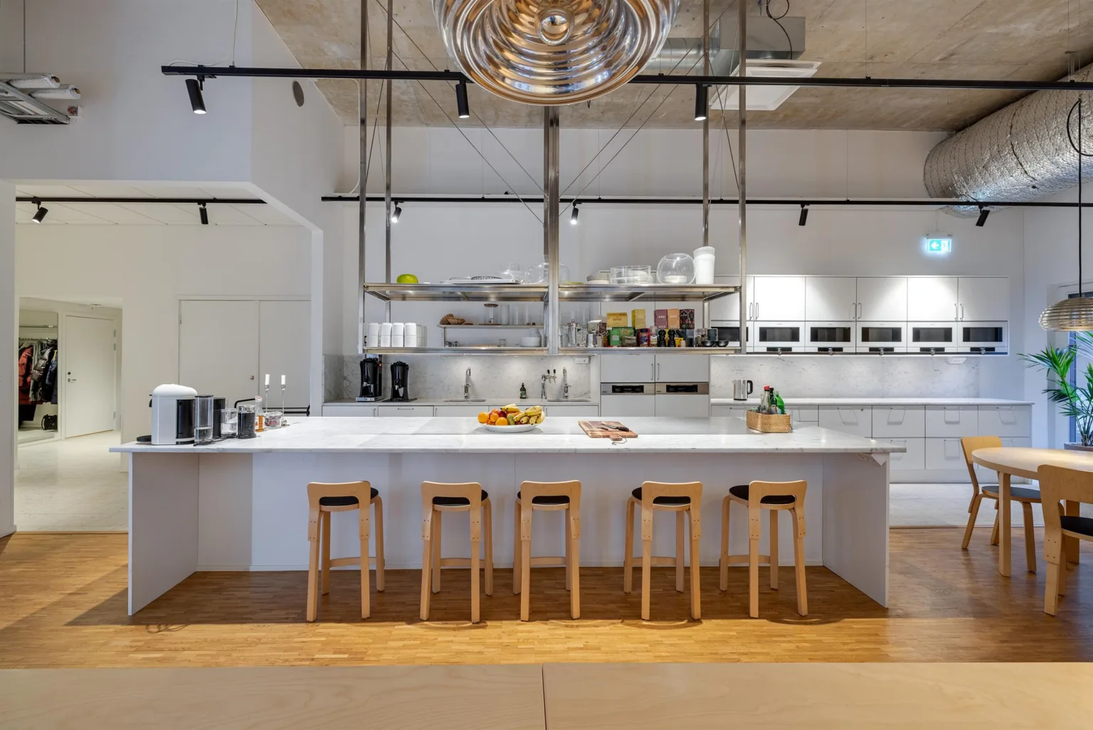 Stilren köksö med fyra träpallar, hyllor med köksutrustning och modern belysning.