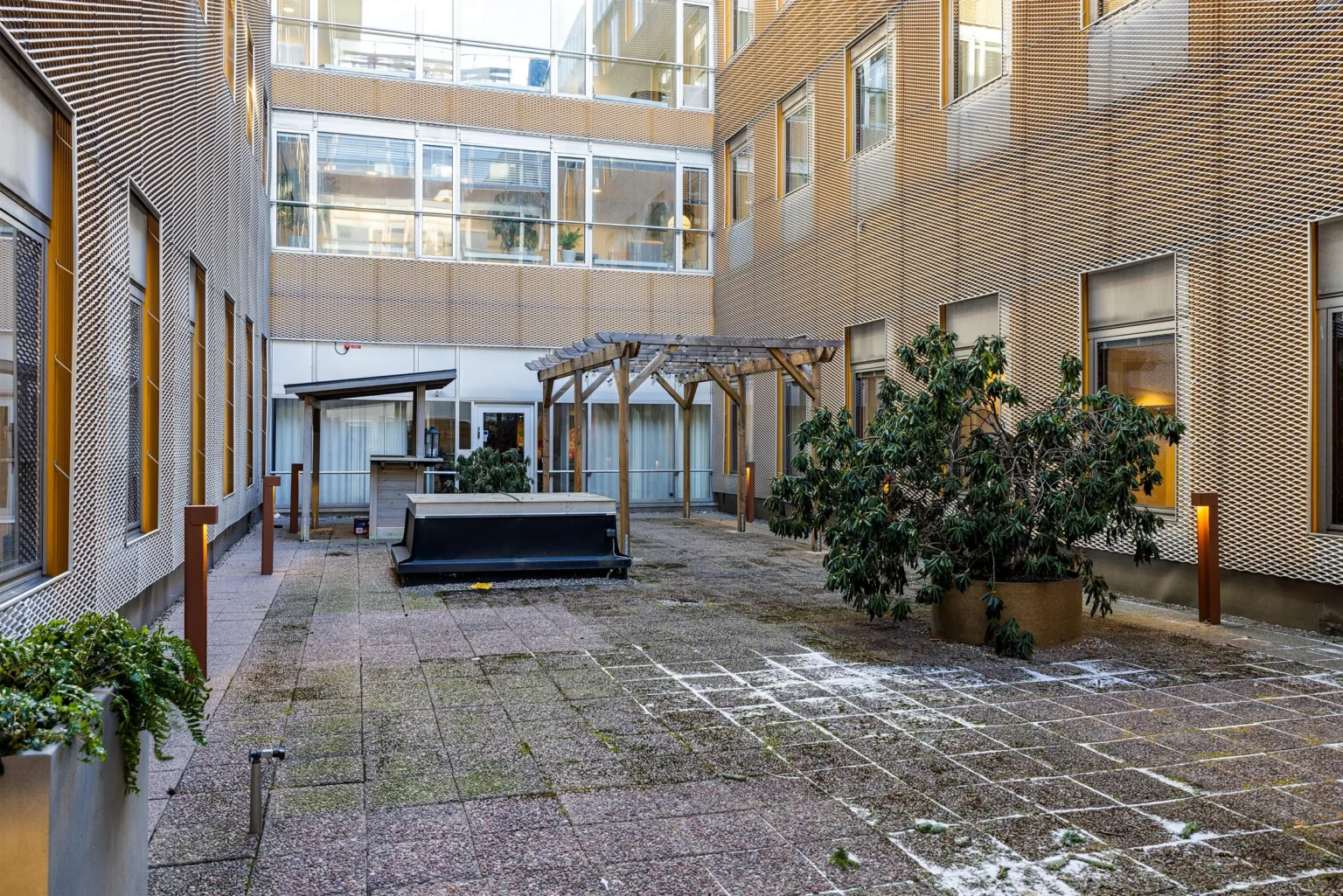 En innergård med stenbeläggning, växter i krukor och byggnadsfasader runtom.