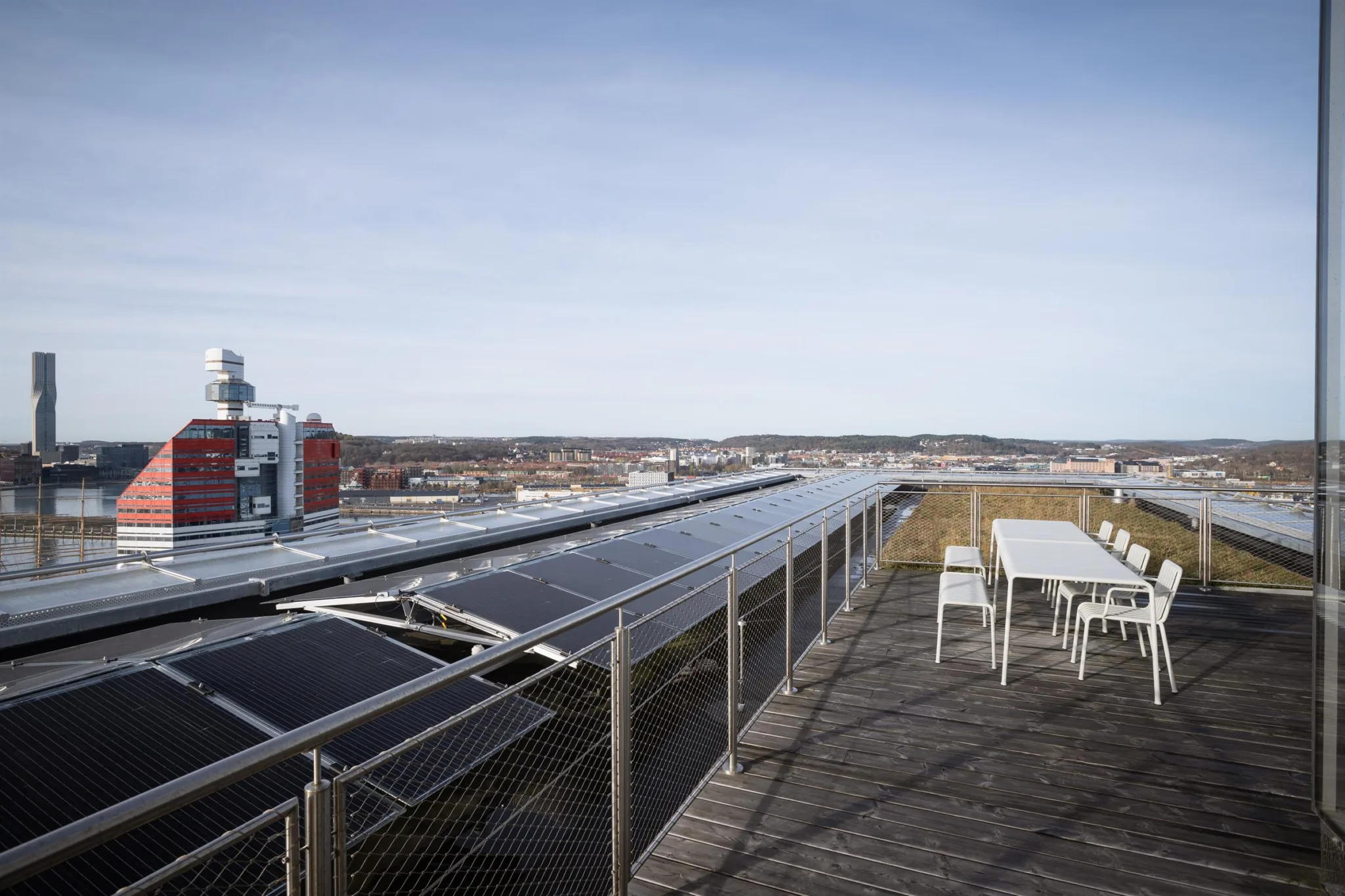 5. En takterrass med solpaneler på ena sidan och vita bord och stolar på andra sidan, med stadsvy i bakgrunden.