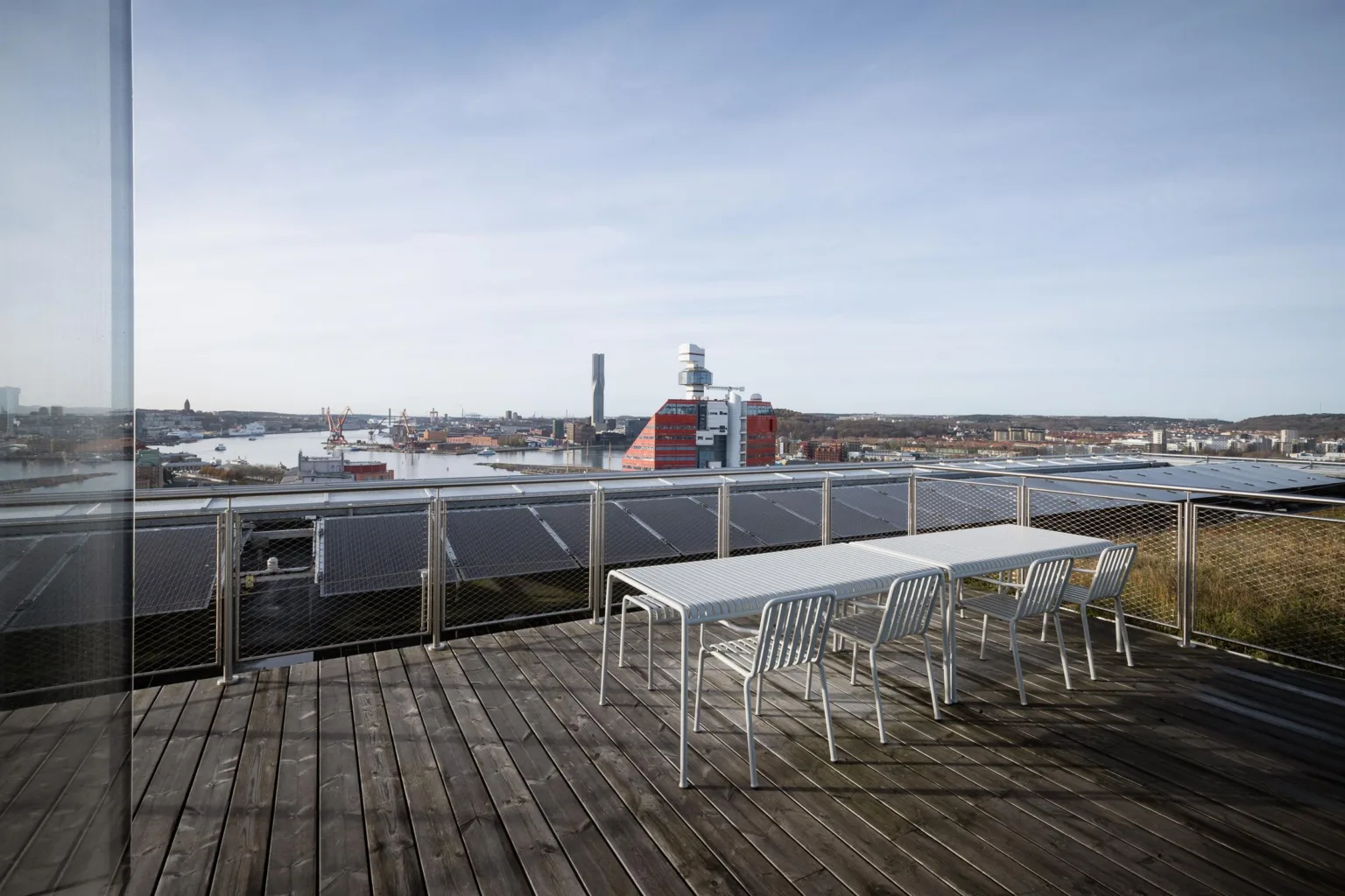 2. En takterrass med vita bord och stolar, med utsikt över en stad och industriella byggnader.