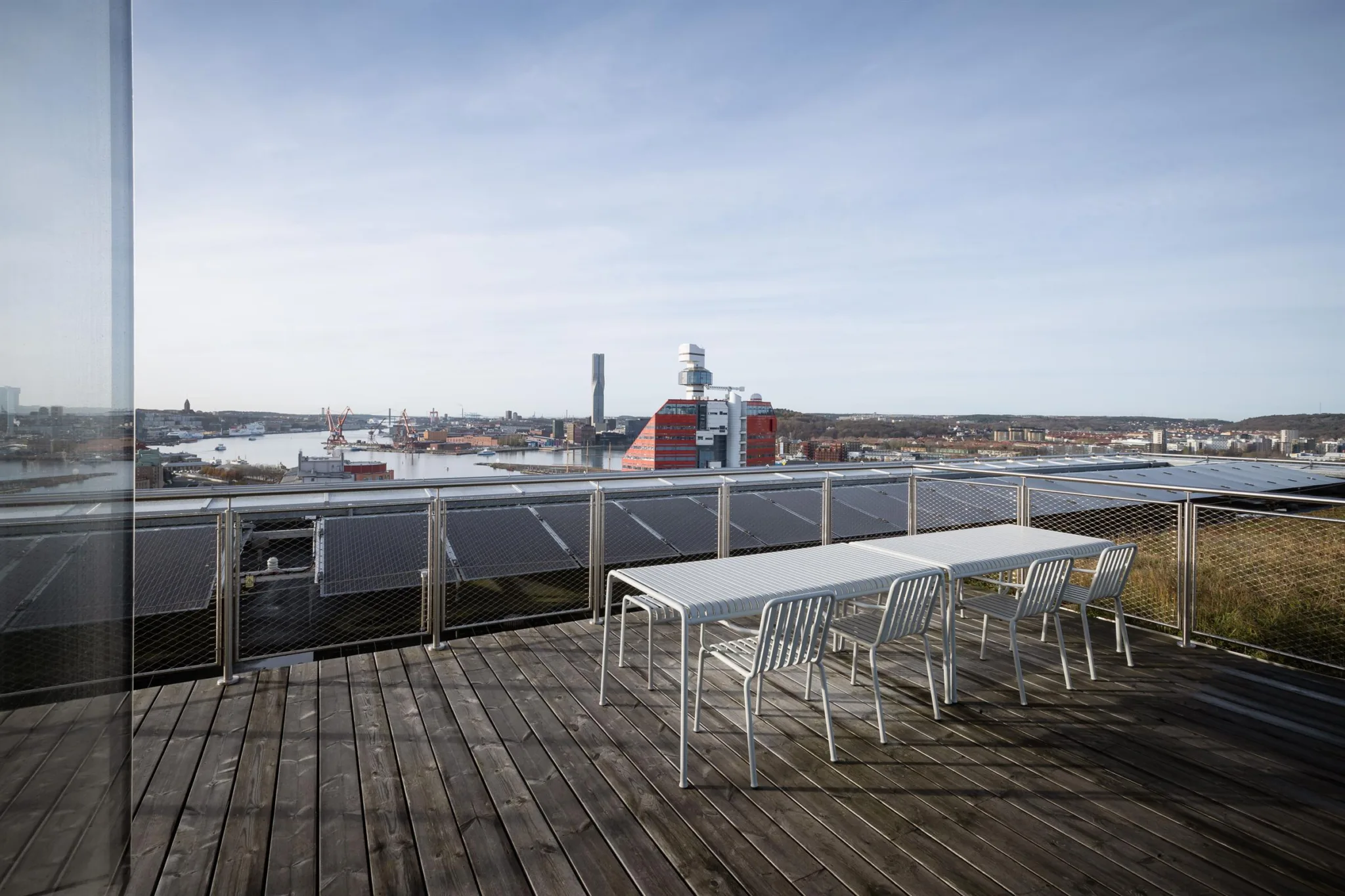 2. En takterrass med vita bord och stolar, med utsikt över en stad och industriella byggnader.