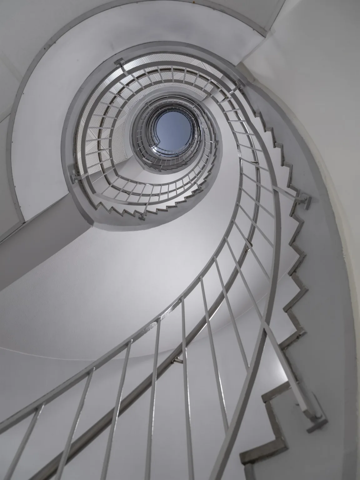 En spiralformad trappa fotograferad uppåt mot ett runt takfönster.